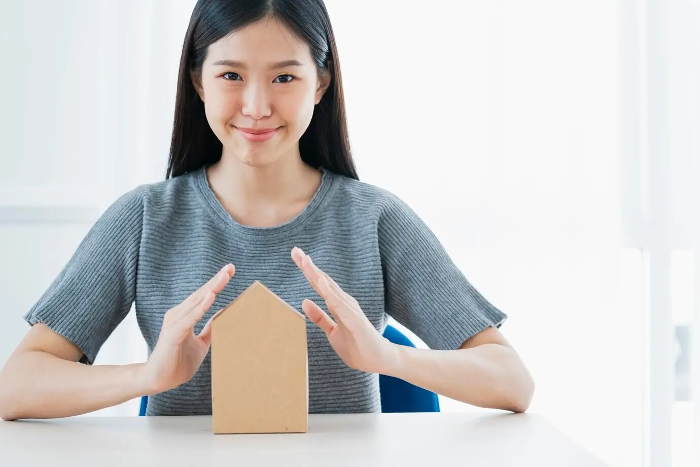 Business insurance ideas concept featuring an Asian woman's hand protecting a paper home model on a white background.